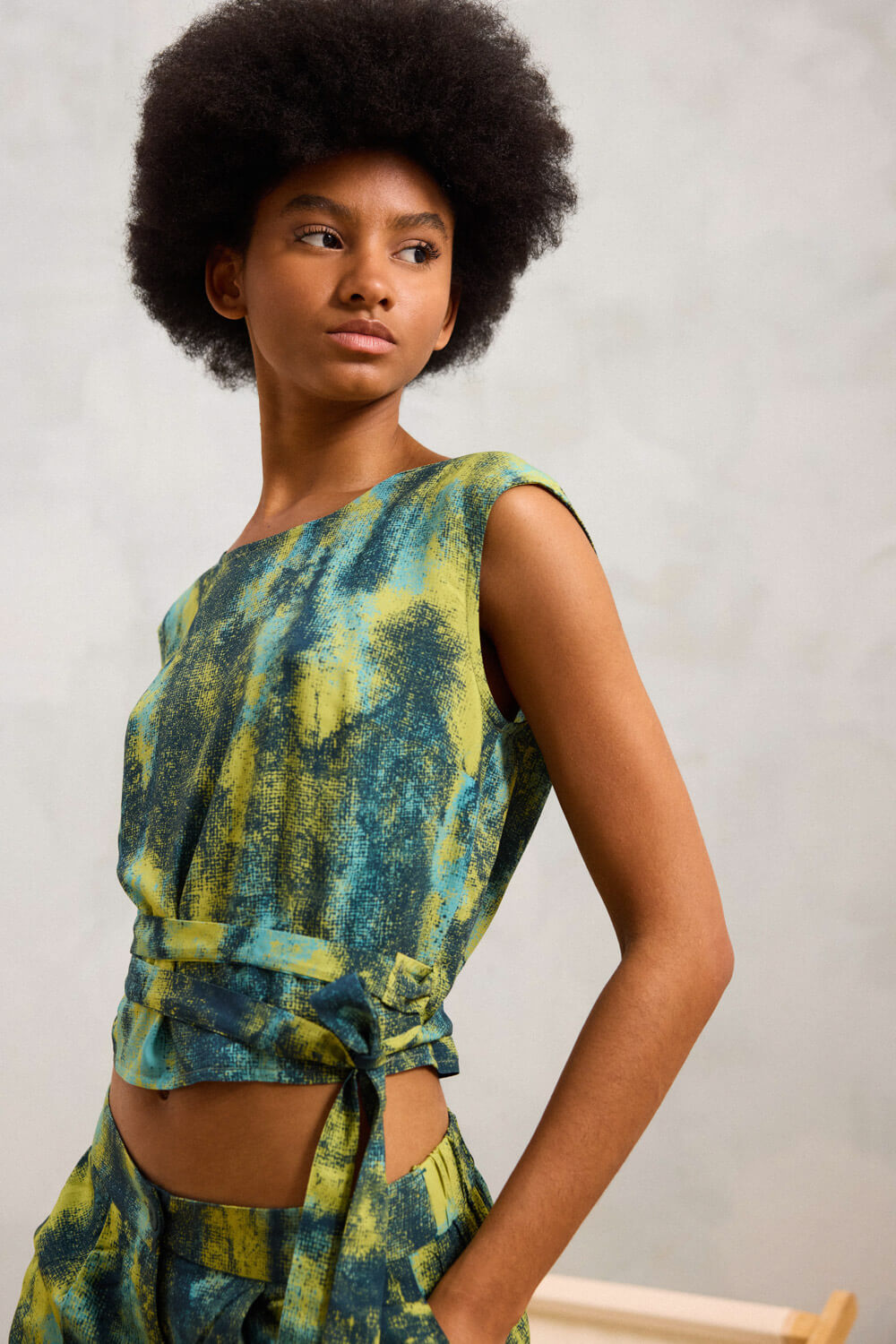 Τουνίκ cropped από μαλακή viscose με στρογγυλή λαιμόκοψη και κοφτά μανίκια που αγκαλιάζουν ελαφρά τους ώμους. Το πίσω μέρος κλέβει τις εντυπώσεις, με κρουαζέ σχέδιο που δένει γύρω από τη μέση, αφήνοντας διακριτικά ανοιχτή την πλάτη. Το ψηφιδωτό print με έντονη χρωματική αντίθεση, προσθέτει δυναμισμό και καλλιτεχνικό χαρακτήρα στο σύνολο. Συνδυάζεται με την παντελόνα BERIT για ένα μοντέρνο και προσεγμένο outfit. Σύνθεση : 100% Βισκόζη Τα ρούχα Namaste σχεδιάζονται και ράβονται στην Ελλάδα. Δωρεάν αποστολή σε 1-3 μέρες σε όλη την Ελλάδα. Διαθέσιμο και στο φυσικό κατάστημα YELLOW BUTTON Χρεμωνίδου & Δαμάρεως 61 Παγκράτι